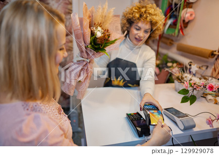 Inside a charming flower shop, a cheerful sales associate assists a customer with a lovely bouquet Inside a charming flower shop, a cheerful sales associate assists a customer with a lovely bouquet 129929078