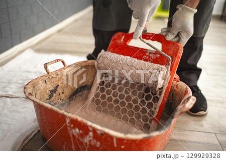 Man dips a paint roller to wipe off the excess paint on the squeegee Man dips a paint roller to wipe off the excess paint on the squeegee 129929328