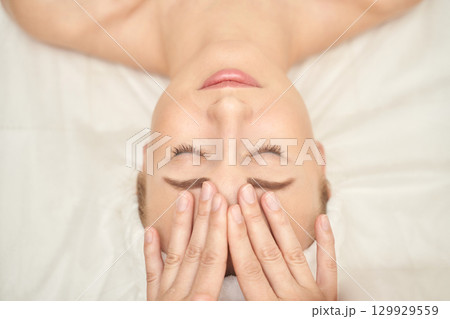 Relaxed caucasian young female receiving facial massage at spa wellness center 129929559