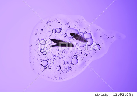 Beautiful texture of gel-like serum with a leaf on a purple background. 129929585