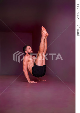 Man holds advanced balance pose on hands with straight lifted legs. Concept of strength, balance, focus, endurance, discipline and physical mastery. Man holds advanced balance pose on hands with straight lifted legs. Concept of strength, balance, focus, endurance, discipline and physical mastery. 129929633