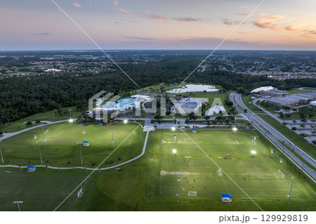 Illuminated public sports arena in North Port, Florida with people playing soccer game on grass football stadium at sunset. Outdoor activities concept 129929819