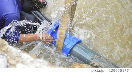 A plumber is repairing a large water pipe that is leaking badly. 129930177