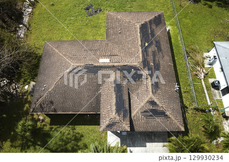 Damaged house roof with missing shingles after hurricane Ian in Florida. Consequences of natural disaster Damaged house roof with missing shingles after hurricane Ian in Florida. Consequences of natural disaster 129930234