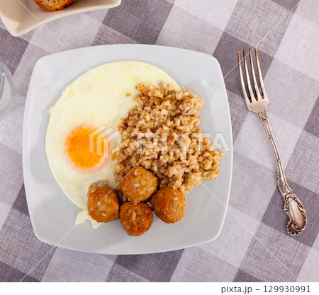 Small portion of oatmeal, stewed meatballs and fried egg 129930991