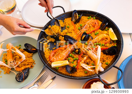 Womens hands lay out sea paella in plates for family dinner 129930993