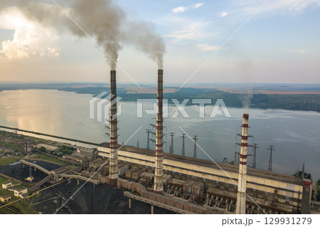 Aerial view of high chimney pipes with grey smoke from coal power plant. Production of electricity with fossil fuel. 129931279