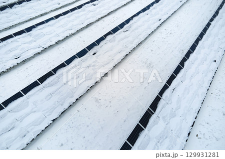 Aerial view of snow covered sustainable electric power plant with rows of solar photovoltaic panels for producing clean electrical energy. Low effectivity of renewable electricity in northern winter Aerial view of snow covered sustainable electric power plant with rows of solar photovoltaic panels for producing clean electrical energy. Low effectivity of renewable electricity in northern winter 129931281