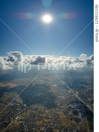 Aerial view from airplane window at high altitude of distant city covered with puffy cumulus clouds forming before rainstorm 129931286
