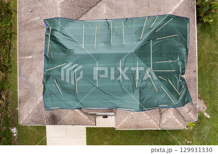 Hurricane damaged house rooftop covered with protective plastic tarp against rain water leaking until replacement of asphalt shingles. Aftermath of natural disaster 129931330