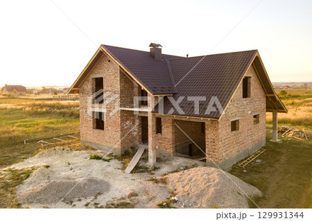 Unfinished brick house with wooden roof structure covered with metal tile sheets under construction. Unfinished brick house with wooden roof structure covered with metal tile sheets under construction. 129931344