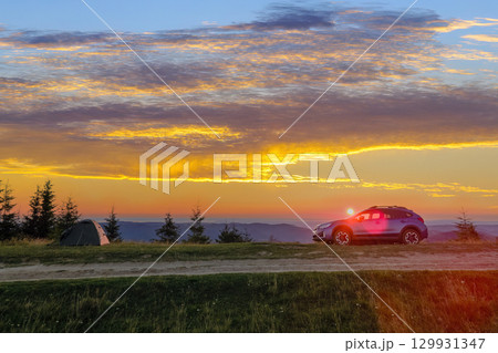 Tourist camping tents and off road car on mountain campsite at bright sunny evening. Active tourism and offroad driving adventure concept Tourist camping tents and off road car on mountain campsite at bright sunny evening. Active tourism and offroad driving adventure concept 129931347