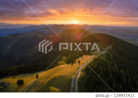 Mountain landscape of trekking route. Dark dirt road between spruce woods illuminated with yellow setting sun. Bright colorful sunset in wild national park highlands Mountain landscape of trekking route. Dark dirt road between spruce woods illuminated with yellow setting sun. Bright colorful sunset in wild national park highlands 129931411