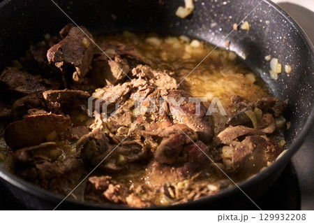 Cooking sliced liver with onions in a frying pan on a stovetop, showcasing the preparation of a hearty dish at home 129932208