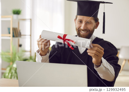 Happy student who has finished online degree is sitting by laptop and holding diploma in hands Happy student who has finished online degree is sitting by laptop and holding diploma in hands 129932495