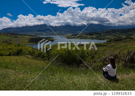 Female tourist sitting looking at the biggest artificial lake in Colombia called Calima Lake located on the mountains of Darien at the region of Valle del Cauca Female tourist sitting looking at the biggest artificial lake in Colombia called Calima Lake located on the mountains of Darien at the region of Valle del Cauca 129932633