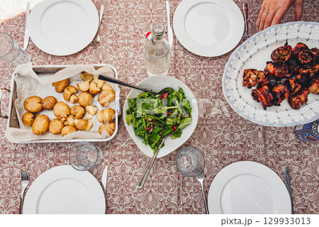 Fresh salad, roasted potatoes and grilled pork belly skewers on table 129933013