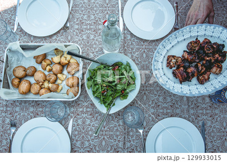Fresh salad, roasted potatoes and grilled pork belly skewers on table 129933015