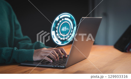 Female user working on a laptop, downloading updates with slow internet from Wi-Fi. Loading symbol highlights delays in file retrieval, reflecting digital software management and connectivity issues. 129933316