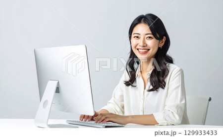 日本人女性が白いデスクでPC作業するライトグレー背景ポートレート 129933433