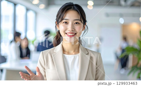 ベージュスーツの日本人女性がオープンオフィスで同僚と会話する笑顔ポートレート ベージュスーツの日本人女性がオープンオフィスで同僚と会話する笑顔ポートレート 129933463
