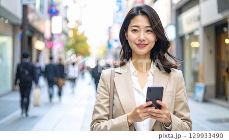 ベージュスーツの日本人女性が通勤中スマホをチェックするポートレート 129933490
