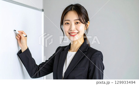 黒のブレザーを着た日本人女性がホワイトボードでビジネス説明 129933494