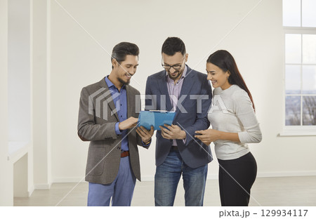 Young happy couple reaching agreement and going to sign a deal with a real estate agent. 129934117
