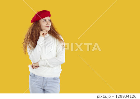 Thoughtful curly girl in red beret and white sweater looking on copyspace on yellow background. Thoughtful curly girl in red beret and white sweater looking on copyspace on yellow background. 129934126