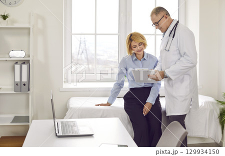 Doctor holding report file with appointment and giving consultation to woman patient in clinic. 129934150