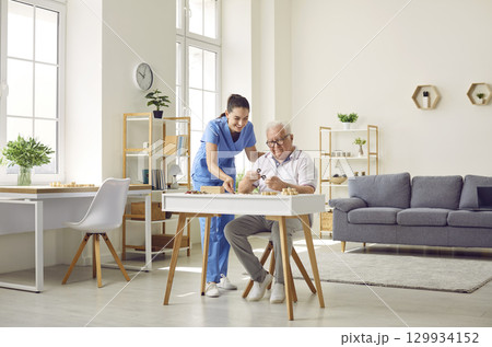 Demented senior man together with nurse playing games and doing puzzles in retirement home 129934152