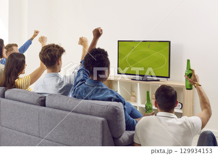 Group of diverse friends sitting on couch, drinking beer and watching soccer on TV 129934153