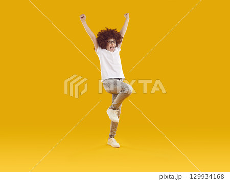Preteen smiling boy happily jumping with his hands raised 129934168