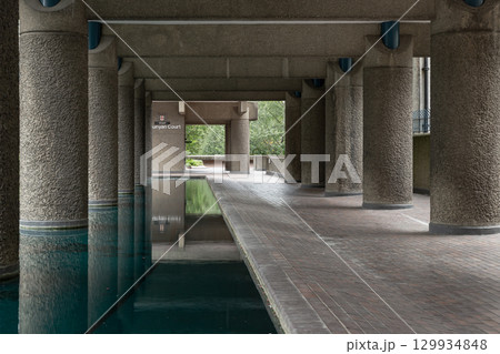the Barbican's design, including the large, textured concrete pillars line, a pathway, and an open area, all contributing to the distinctive aesthetic of brutalist design. 129934848