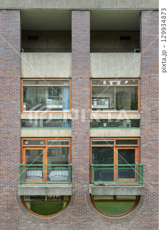 Residential units within the Barbican Estate, characterized by windows integrated with small balconies featuring green metal railings and prominent exposed brickwork. 129934873