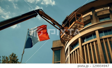 A cherry picker lift stands by a building with the French flag in the foreground, symbolizing repair, construction, or renovation concepts in France 129934947
