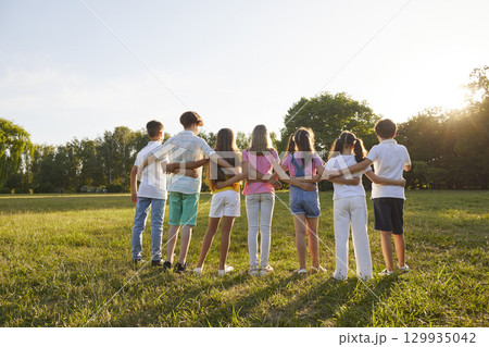 Group of teenage children look at sunset together during summer walk in green park. 129935042