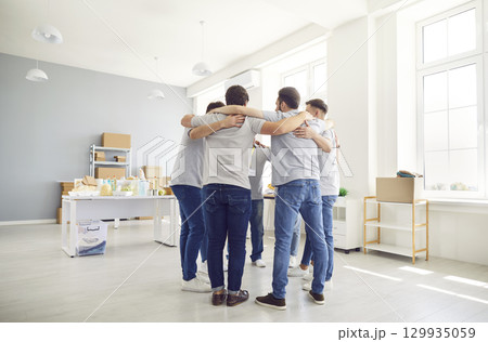 Group of volunteers standing together in circle and hugging during work in humanitarian center. Group of volunteers standing together in circle and hugging during work in humanitarian center. 129935059