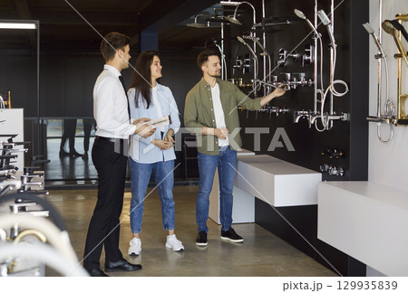 The salesman assists a young couple to choose a tap or faucet for home. The salesman assists a young couple to choose a tap or faucet for home. 129935839