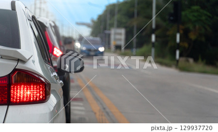 Rear side of white car with turn on brake light. Cars parked in a queue waiting for the traffic light. Traffic line on the side of the road. Cars on opposite side are waiting for the traffic light. 129937720