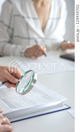 Team of accountants are working together, using a magnifying glass and a calculator, to audit financial reports in office. Audit and taxes concept 129938702