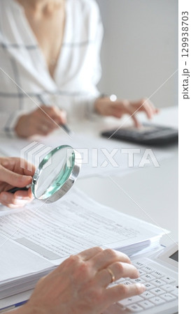 Team of accountants are working together, using a magnifying glass and a calculator, to audit financial reports in office. Audit and taxes concept 129938703