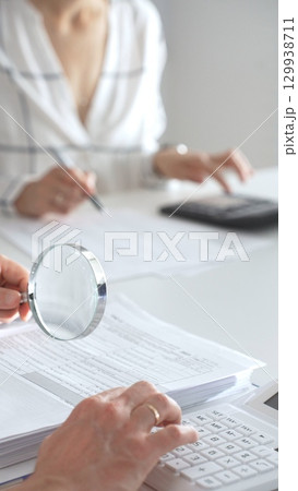 Two accountants are working together, using a magnifying glass and a calculator, to audit financial reports in their brightly lit office. Audit and taxes in business Two accountants are working together, using a magnifying glass and a calculator, to audit financial reports in their brightly lit office. Audit and taxes in business 129938711