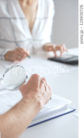 Close up of accountant hand using a magnifying glass and a calculators, to audit financial reports in brightly lit office. Audit and taxes concept Close up of accountant hand using a magnifying glass and a calculators, to audit financial reports in brightly lit office. Audit and taxes concept 129938726