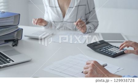 Accounting team collaborating, reviewing financial reports, using calculator, analyzing data while working at sleek corporate workspace. Audit and taxes in business 129938728