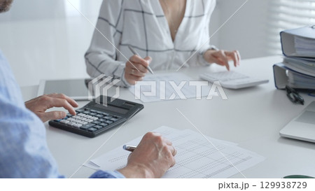 Accounting team collaborating, reviewing financial reports, using calculator, analyzing data while working at sleek corporate workspace. Audit and taxes in business Accounting team collaborating, reviewing financial reports, using calculator, analyzing data while working at sleek corporate workspace. Audit and taxes in business 129938729