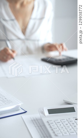 Close up of a calculator on financial documents, with an accountant taking notes, emphasizing accounting, finance, and tax preparation. Audit and taxes in business 129938772