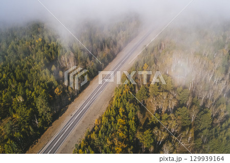 Aerial view of a winding road through green landscapes and fog-covered valleys under a clear blue sky Aerial view of a winding road through green landscapes and fog-covered valleys under a clear blue sky 129939164