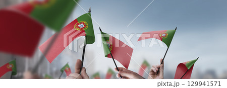 Portugal flags in their hands on a blurred urban background Portugal flags in their hands on a blurred urban background 129941571