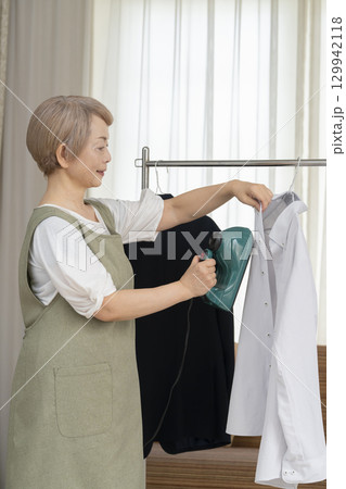 リビングでハンガーに掛けた衣類にスチームアイロンをかけるシニア リビングでハンガーに掛けた衣類にスチームアイロンをかけるシニア 129942118